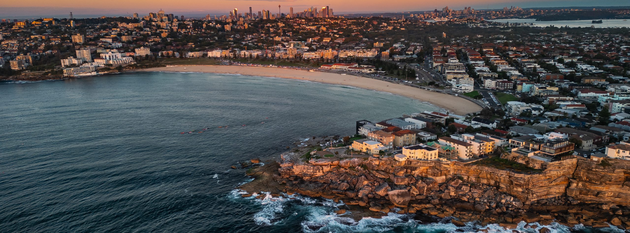 Aerial view of a city and beach at sunset, showcasing vibrant colours reflecting on the water and skyline.