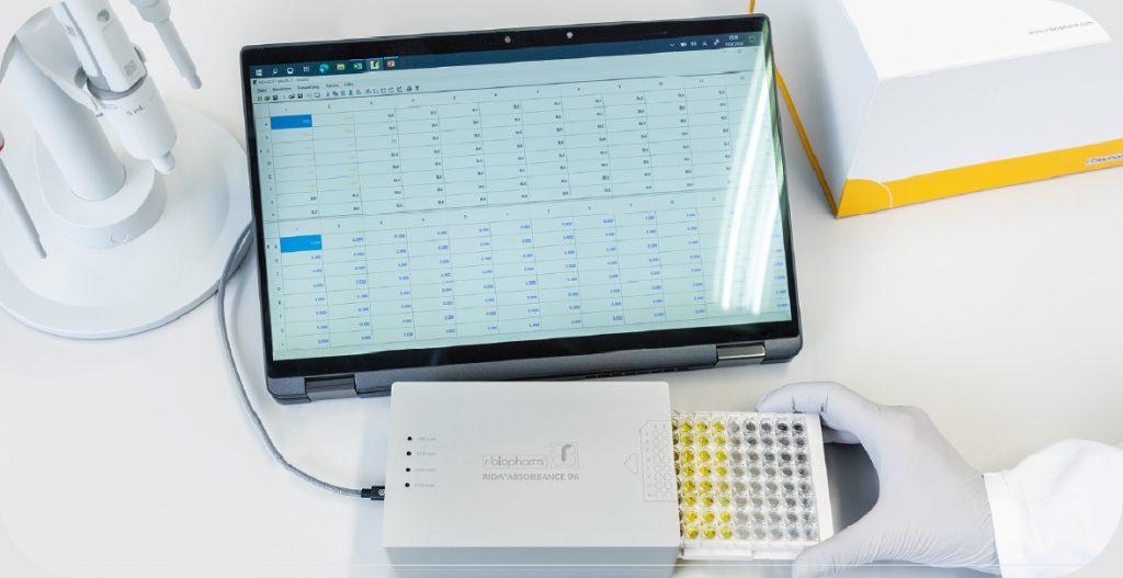 a scientist holds a small rectangular piece of equipment connected to a computer